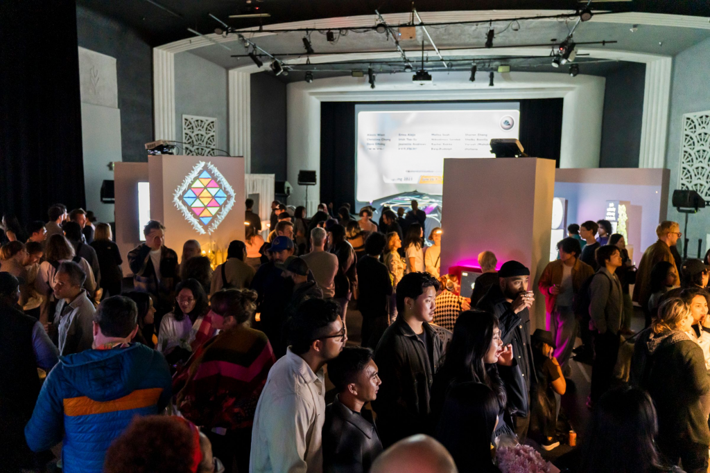 photo of a large crowd in the gray area foundation theater location, dimly-lit and surrounded by colorful digital art projections